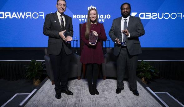 Three people holding awards in front of a screen that reads "forward-focused" 